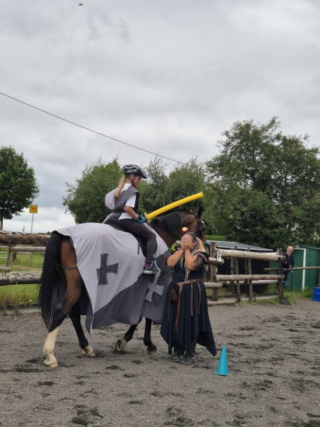 Reiter in Ritterrüstung auf einem Pferd, während eine Person daneben steht.